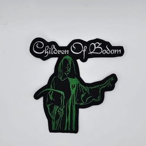 Könnte beinhalten: Schwarz-grüner, gestickter Aufnäher mit dem weißen Schriftzug "Children Of Bodom". Das Design zeigt eine Kapuzenfigur mit ausgestreckten Armen. Geeignet für Kleidung oder Accessoires.
