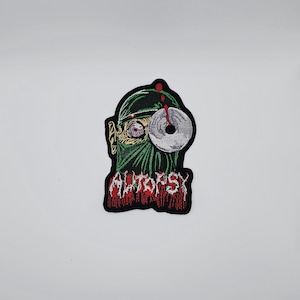 Puede incluir: Parche bordado que representa una figura enmascarada de verde con un instrumento quirúrgico y la palabra "AUTOPSY" en rojo. El parche tiene un borde negro y está diseñado con un tema de terror.