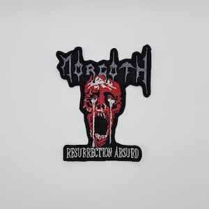 May include: Embroidered patch with the word "Morgoth" in grey above a red, screaming face with white tears. The text "Resurrection Absurd" is below the face in a black rectangle. The patch has a black border.