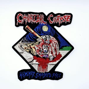 May include: Embroidered patch featuring the words "Cannibal Corpse" in red above a graphic of a skull being struck with a hammer. The words "Hammer Smashed Face" are embroidered in blue below the graphic. The patch is black with a white background.