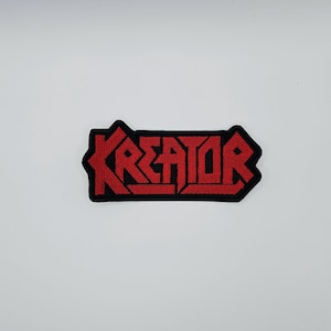Könnte beinhalten: Ein rechteckiger Aufnäher mit dem Wort "KREATOR" in roter, gestickter Schrift. Der Aufnäher hat einen schwarzen Rand und ist vor einem weißen Hintergrund platziert. Das Design ist auffällig und markant.