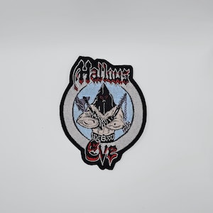 May include: Embroidered patch with a hooded figure and chains, set in a circular design. The patch features the text "Hallows Eve" in a gothic font, with red and black detailing. The background is light blue and grey.