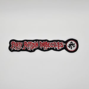 Könnte beinhalten: Ein schwarzer, gestickter Aufnäher mit dem Schriftzug "DIRTY ROTTEN IMBECILES" in roter, gezackter Schrift. Der Aufnäher zeigt auch ein rundes Emblem mit einer rennenden Strichfigur. Zum Aufnähen auf Kleidung oder Taschen.
