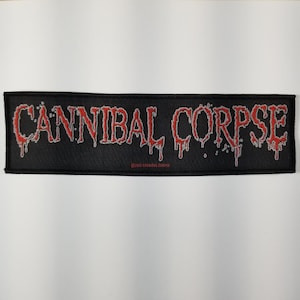Puede incluir: Parche tejido negro con las palabras "Cannibal Corpse" en blanco con pintura roja goteando. El texto tiene copyright 2007 Cannibal Corpse.