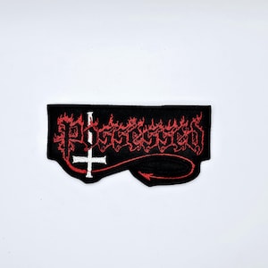 May include: Black embroidered patch with the word "Possessed" in red, stylized lettering. A white upside-down cross is centered, with a red devil's tail extending to the right. The patch is rectangular with a curved bottom edge.