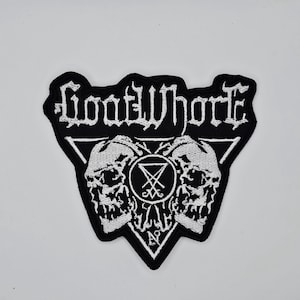 Op de afbeelding: Zwart en wit geborduurde patch met de bandnaam "Goatwhore" in een gotisch lettertype. De patch bevat twee schedels, een pentagram en andere occulte symbolen. De patch heeft een driehoekige vorm.