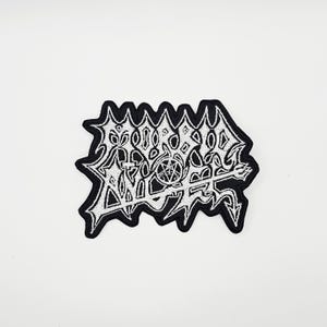 May include: Embroidered patch with a black border and white design. The design features stylized text and a pentagram, with a trident at the bottom. The patch has a jagged, irregular shape.