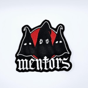 Op de afbeelding: Geborduurde patch met drie zwarte gehoodde figuren tegen een rode achtergrond. Het woord "mentors" is geschreven in witte gotische letters. De patch heeft een witte rand.