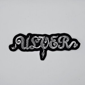 May include: A black and white embroidered patch with the word "ULCER" in a stylized font. The white lettering has a snake-like design, and the patch has a black border.