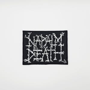 Peut inclure: Écusson rectangulaire noir avec le texte blanc brodé « NAPALM DEATH ». Le texte a une apparence irrégulière et déformée. L'écusson est probablement destiné aux vêtements ou aux accessoires.
