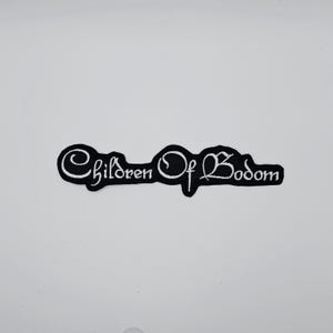 Könnte beinhalten: Schwarz-weißer, gestickter Aufnäher mit dem Schriftzug "Children Of Bodom" in einer stilisierten, kursiven Schrift. Der Text ist schwarz umrandet und weiß gefüllt, was einen starken Kontrast erzeugt. Der Aufnäher ist rechteckig mit abgerundeten Kanten.
