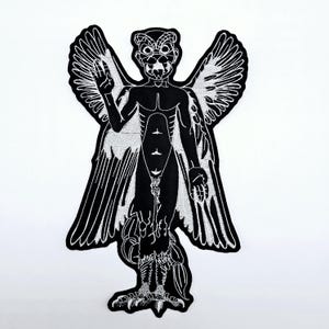 May include: Black and white embroidered patch featuring a stylized winged humanoid figure with a bird-like head. The figure has outstretched wings, a detailed torso, and bird-like feet. The design is outlined in white.
