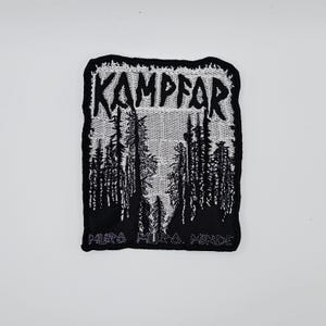 Könnte beinhalten: Ein schwarz-weißer Aufnäher mit dem Wort "KAMPFAR" oben, über einer Waldsilhouette. Der Aufnäher hat einen schwarzen Rand und den Text "MURA. MILA. MINDS" am unteren Rand. Das Design ist eine stilisierte Illustration.
