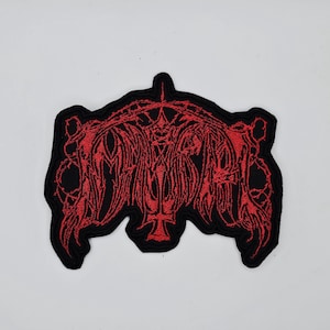 May include: Embroidered patch with a black border and a red, gothic-style design. The patch features an intricate, stylized text and a cross symbol. The design is detailed and appears to be machine-embroidered.