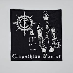 May include: Black square patch with white graphic of a figure, a wheel-like symbol, and text. The text reads "Carpathian Forest" in a gothic font. The patch is likely for clothing or accessories.