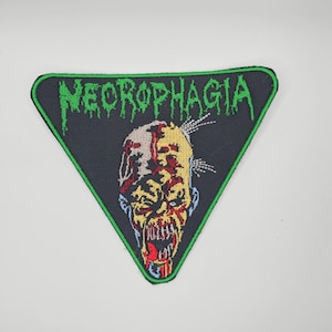 Może przedstawiać: Trójkątna naszywka z motywem zombie i napisem "NECROPHAGIA" w zielonych, ociekających literach. Zombie ma odsłonięte zęby, czerwoną krew oraz żółtą i niebieską skórę. Naszywka ma czarne tło i zieloną obwódkę.
