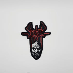 May include: Black and red embroidered patch with the text "SADISTIC INK" in a gothic font. The patch features a stylized face at the bottom. The patch is likely for a jacket or bag.