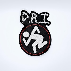Könnte beinhalten: Schwarzer Aufnäher mit den weißen Buchstaben "D.R.I." über einem schwarzen Kreis mit rotem Rand. Im Kreis befindet sich eine weiße Strichmännchen-Figur. Der Aufnäher ist für Kleidung oder Accessoires.