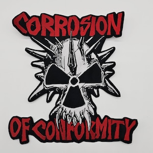 Könnte beinhalten: Ein schwarz-weißer Aufnäher mit einem Totenkopf-Design, Stacheln und den Worten "CORROSION" und "OF CONFORMITY" in roter, stilisierter Schrift. Der Aufnäher hat einen schwarzen Rand und ist wahrscheinlich für Kleidung oder Accessoires.