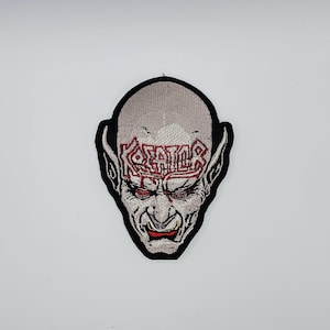 Op de afbeelding: Geborduurde patch met een demonisch gezicht met rode ogen en mond. Het woord "KREATOR" is in het rood op het voorhoofd geborduurd. De patch heeft een zwarte rand op een witte achtergrond.