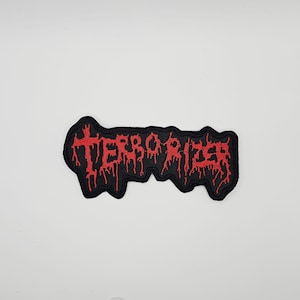 May include: A black embroidered patch with the word "TERRORIZER" in dripping red letters. The patch has a jagged, irregular shape and is likely designed to be sewn or ironed onto clothing or accessories.