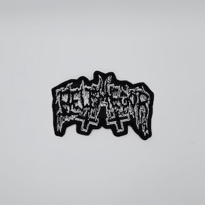 Puede incluir: Parche bordado en blanco y negro con la palabra "DEATH" en una fuente gótica. El parche presenta dos cruces invertidas y un borde dentado. El parche es probablemente para una chaqueta o bolso.