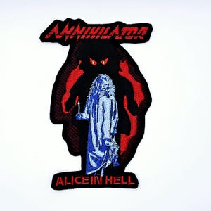 May include: Embroidered patch with the word "ANNIHILATOR" in red, above a black silhouette with red accents. The silhouette frames a blue figure holding a candle, with the text "ALICE IN HELL" below.