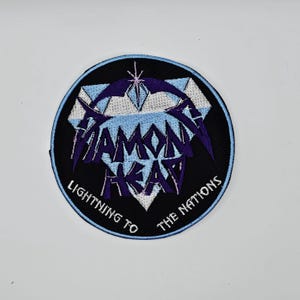 Könnte beinhalten: Ein runder, schwarzer, gestickter Aufnäher mit dem Schriftzug "Diamond Head" in Lila und Weiß sowie dem Text "Lightning to the Nations" in Weiß. Der Aufnäher hat ein geometrisches Design in Hellblau und Lila mit einem blauen Rand.