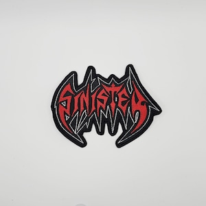 May include: Embroidered patch with the word "SINISTER" in red, stylized lettering. The patch has a black border and white accents, set against a white background. The design has a gothic or heavy metal aesthetic.