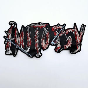 Może przedstawiać: Czarna, haftowana naszywka z napisem "ANGRY" w stylizowanej, gotyckiej czcionce. Litery są czerwone i białe, z łańcuchem i postarzaną fakturą. Przeznaczona do odzieży lub akcesoriów.