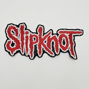 May include: An embroidered patch featuring the word Slipknot in a jagged, stylized red font with a white outline and a thick black border. The lettering has a distressed, rough-edged appearance, creating a bold graphic design element.