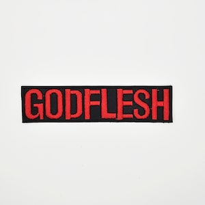 May include: A rectangular black patch with the word "GODFLESH" embroidered in red block letters. The patch has a red border and is set against a white background.