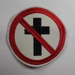 May include: A red circle with a white background and a black cross with a red line through it. The cross is in the centre of the circle. The circle has a white border.