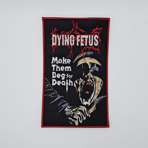Puede incluir: Parche rectangular negro con borde rojo. Presenta el texto "DYING FETUS" en rojo, con una fuente estilizada. Debajo, se muestra el texto "Make Them Beg for Death". También hay una ilustración de una figura gritando.