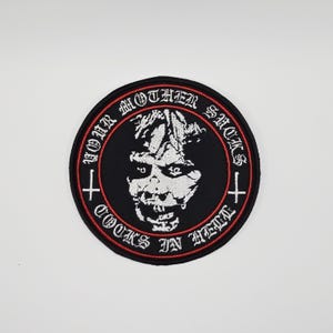 May include: Round black patch with a white, stylized demonic face in the center. The patch has a red border and the text "YOUR MOTHER SUCKS" and "COOKS IN HELL" in white, gothic lettering. Two white crosses are on the sides.