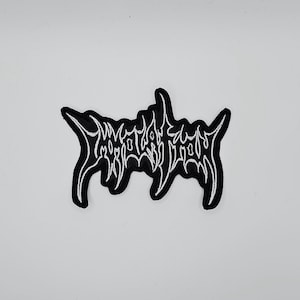 May include: Black and white embroidered patch with stylized text. The patch has a black background with white stitching forming the text. The text is in a gothic or heavy metal style font.