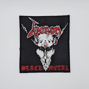 以下が含まれることがあります： 赤と白の「Venom」の文字と、角のある白い頭蓋骨のイラストが描かれた黒いパッチ。頭蓋骨の下には「BLACK METAL」の文字が赤で書かれています。パッチは正方形で、黒い縁取りがあります。