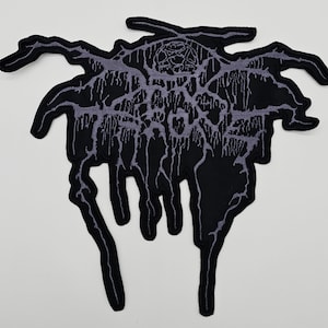 以下が含まれることがあります： ユニークな抽象的なデザインの、黒とグレーの刺繍パッチ。パッチは、複雑なディテールと滴るような有機的な形状を持つ中央のエンブレムが特徴です。配色パターンは主に黒とグレーのアクセントで、印象的なコントラストを生み出しています。