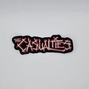Könnte beinhalten: Schwarzer, gestickter Aufnäher mit dem Text "THE CASUALTIES" in weißer, handschriftlicher Schrift, umrandet in Rot. Der Aufnäher hat einen schwarzen Rand und ist für Kleidung oder Accessoires bestimmt.