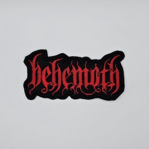 May include: A black embroidered patch with the word "behemoth" in red gothic lettering. The patch has a black border and is likely designed to be sewn or ironed onto clothing or accessories.