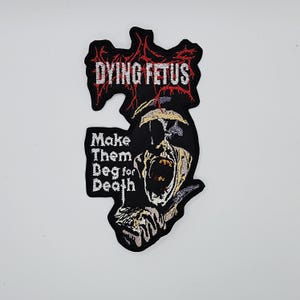 Peut inclure: Écusson brodé noir avec le texte "DYING FETUS" en rouge et blanc, au-dessus de la phrase "Make Them Beg for Death". L'écusson présente un motif de crâne hurlant.