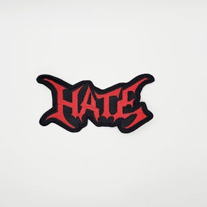 Puede incluir: Parche bordado con la palabra "HATE" en rojo, con letras de estilo gótico. El parche tiene un borde negro y está diseñado para planchar o coser en ropa o accesorios.