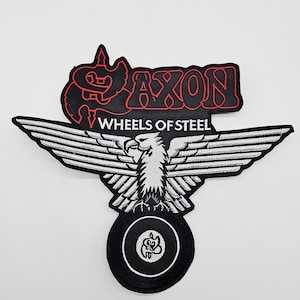 Op de afbeelding: Zwart-witte geborduurde patch met een adelaar met uitgespreide vleugels en de rode tekst "SAXON WHEELS OF STEEL". De adelaar staat boven een zwart wielontwerp. Geschikt voor kleding.