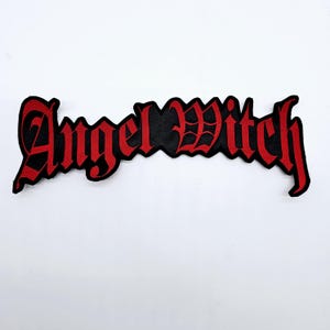 Pode incluir: Um patch bordado preto e vermelho com as palavras "Angel Witch" em uma fonte gótica. O patch tem um fundo preto com letras vermelhas e uma borda preta. O patch é retangular e foi projetado para ser costurado em roupas ou acessórios.