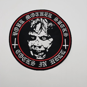 May include: Round black patch with a white, grotesque face in the center. The patch has a red border and white text that reads "YOUR MOTHER SUCKS" and "COCKS IN HELL" around the edge. Two white crosses are on either side.