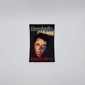 Op de afbeelding: Zwart geborduurde patch met een gestileerd portret met een gespleten gezicht. De tekst "Brujeria" staat bovenaan, met "Matando Güeros" in het rood onderaan. De patch is rechthoekig.