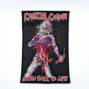 Puede incluir: Parche rectangular negro con el nombre de la banda "Cannibal Corpse" en rojo, sobre una ilustración de un zombi. El texto "Eaten Back to Life" está debajo, también en rojo. El zombi se representa con órganos expuestos.