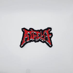 Op de afbeelding: Geborduurde patch met het woord "ATHEIST" in rode, gestileerde, gotische letters. De patch heeft een zwarte rand en witte accenten in de letters. Geschikt om op kleding of tassen te naaien.