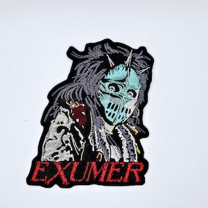 May include: Embroidered patch with a detailed design of a figure wearing a teal mask and spiky headgear. The figure is set against a black background with the word "EXUMER" in red lettering at the bottom. The patch has a unique, detailed design.