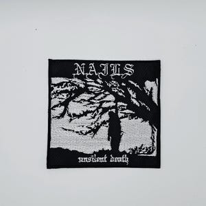Könnte beinhalten: Schwarz-weißer, gestickter Aufnäher mit dem Wort "NAILS" in gotischer Schrift über einer Silhouette unter einem Baum. Der Satz "unsilent death" befindet sich unter dem Bild.